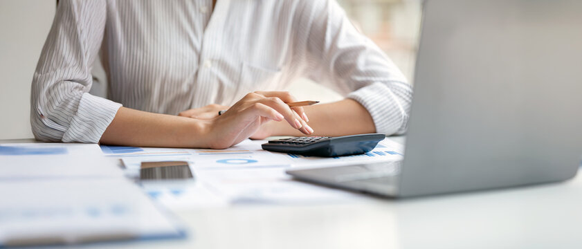 A professional is working at a modern office desk, using a calculator and a laptop with financial documents spread out.