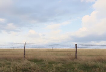 Fototapeta premium Serene Prairie: Wire Fence, Golden Grass, and Soft Cloudscape