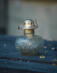 A beautifully crafted vintage glass oil lamp sits on a weathered wooden table. The intricate design...