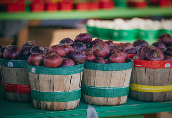 Rustic baskets filled with vibrant red onions are neatly arranged at a market stand. The green trim on the baskets complements the overall scene.