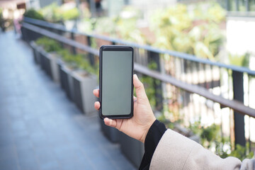 Holding a phone on a sunny outdoor walkway