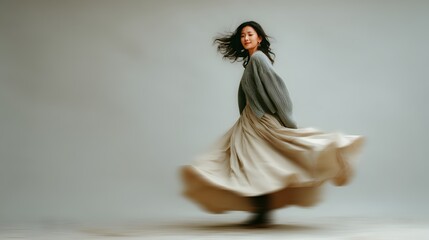Asian woman in a flowing skirt twirling against a plain background. Motion blur captures the movement of the skirt, soft and elegant, autumn fashion 