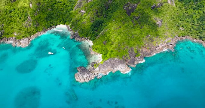 A vibrant coastal landscape with lush green hills meeting the bright turquoise waters, offering a stunning natural view. Seychelles, Mahe.