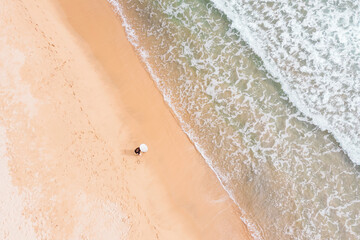 Woman holding surfboard on beach with sea in background, aerial view.