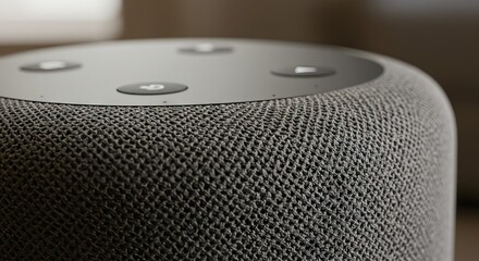 Closeup of a gray cylindrical smart speaker with a woven fabric exterior and black circular buttons on top