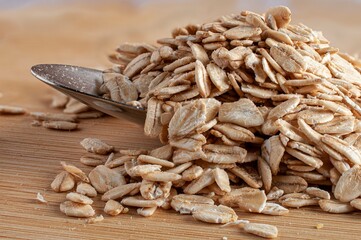 Macro photography of a spoon with raw or uncooked oats on a wooden cutting board, horizontal image