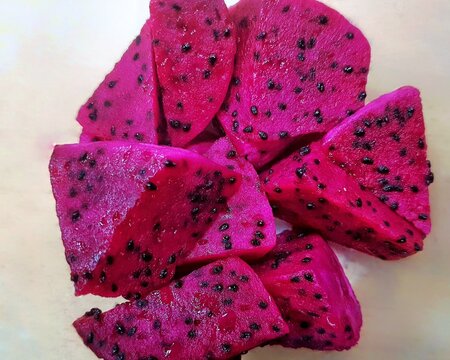 Fresh sliced dragon fruit with vibrant pink flesh and black seeds on neutral background