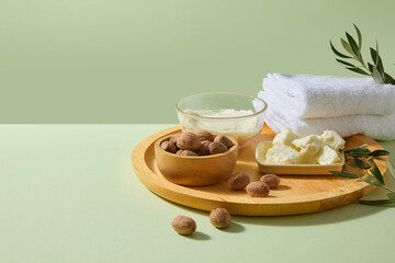 Rustic wooden tray holding ivory shea butter, scattered smooth shea nuts and soft sprigs on neutral fabric, ideal for handmade body butter or organic spa promotions. Front view, space for add text.