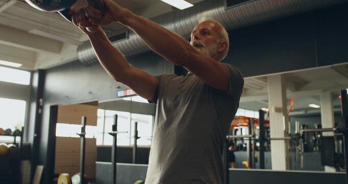 Fit mature man in sportswear
swinging a kettlebell during a weight
training session in a gym