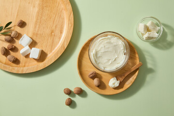 Soft daylight highlights shea butter scoops, rustic spoon and scattered nuts on pale green background, leaving blank area for overlay text or natural product marketing. Top view