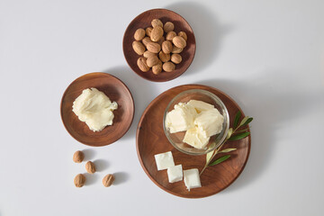 Overhead composition of shea butter scoops, nuts and wooden dishes on white background, leaving...