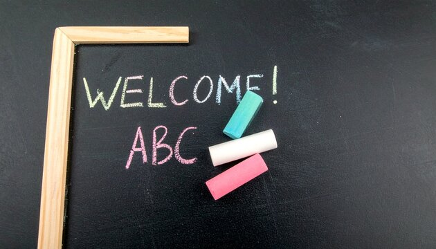 A blackboard with the word welcome and ABC written in chalk, next to colorful chalk pieces.