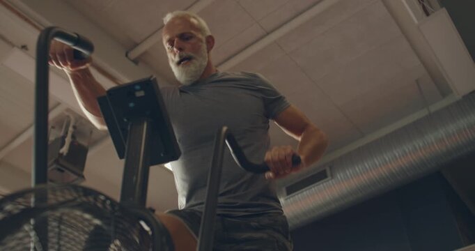Low angle view of a fit mature man in
sportswear working out on a
stationary bike at the gym