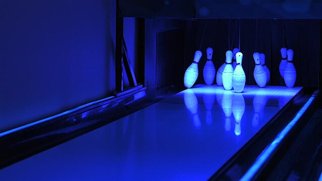Resetting bowling pins under neon lighting after a strike, glowing pins reflecting on the lane. Captured in 4K slow motion.