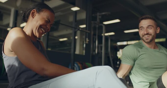Two diverse fit young people talking and
laughing while sitting on a gym floor
after an exercise class