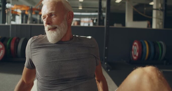 Fit mature man sitting on a gym floor
and talking with others after a
workout session