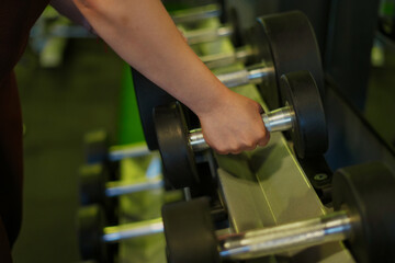 Fototapeta premium Person reaching for a dumbbell in gym for workout
