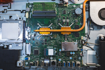 Close-up image of an all-in-one computer interior showing the motherboard, heat pipe cooling system, RAM slot, processor, and electronic components. Inside View of All-in-One Computer Motherboard
