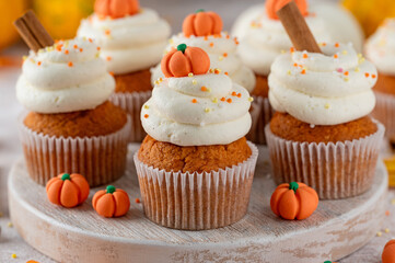 Pumpkin spice cupcakes decorated butter cream frosting, sugar sprinkles and mini sweet pumpkins on top. Thanksgiving or Halloween dessert.