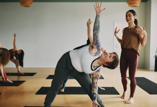 Smiling young female yoga teacher encouraging a young woman with tattoos during a class with others in her studio