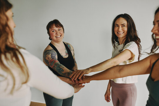 Smiling group of young woman in sportswear standing in a circle with their hands together before a yoga class together