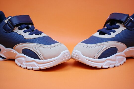 Colorful kids' sneakers displayed creatively on an orange background, showcasing modern design and fashion-forward appeal for children’s footwear in vibrant hues.