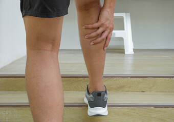 Asian male athlete grips sore calf post-run on stairs—possible gastrocnemius strain or DOMS. Sports injury, muscle pain, recovery, biomechanics.