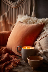 Cozy autumn scene with a lit candle in a mug and decorative pillows.