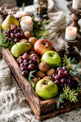 Festive fruit arrangement with candles and walnuts in a wooden tray.
