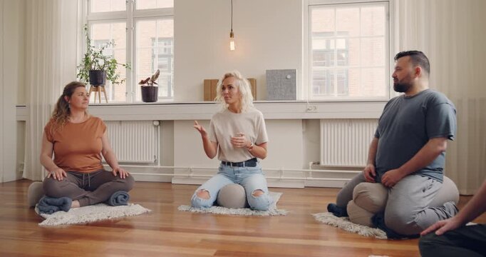 Instructor talking with a mixed age range group
of students before a beginners yoga class in a
studio