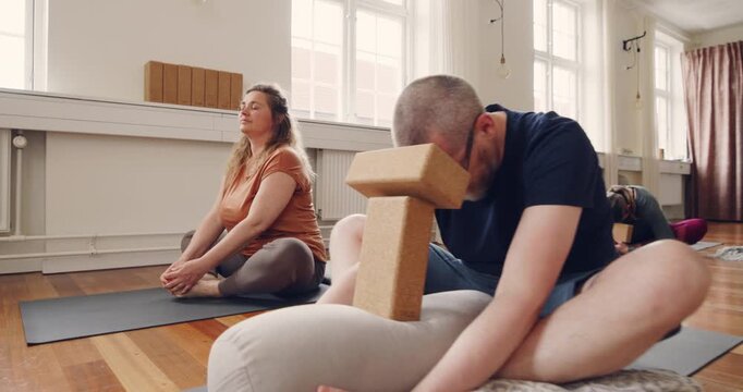 Male beginner student sitting on a studio floor
during a beginners yoga class and using blocks
to help with support