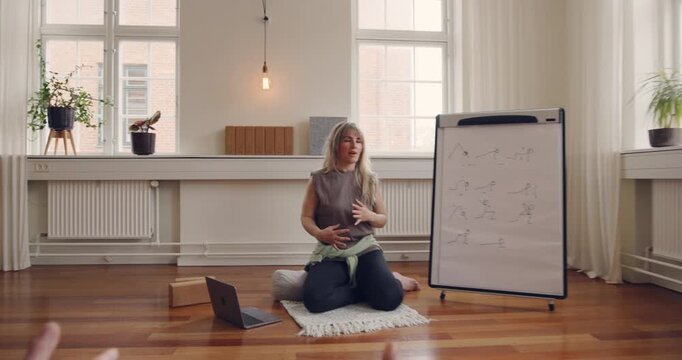 Yoga teacher leading a diverse group of
students through breathing exercises during a
beginners class in her studio