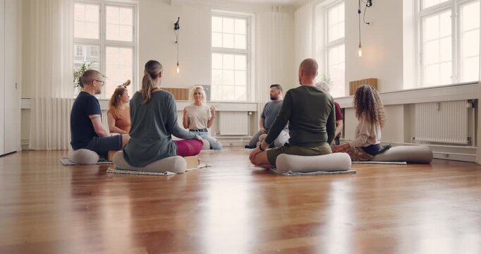 Instructor talking with a mixed age range group
of students sitting on a studio floor before a
beginners yoga class