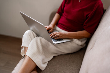 Naklejka premium Older Asian woman works from home using laptop computer on sofa modern living room digital connectivity