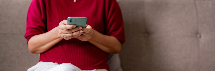 Senior Asian woman hands operating smartphone engaging with modern digital mobile technology for communication online at home cozy living space