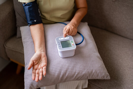 Older Asian woman health monitoring home blood pressure check daily wellness routine hypertension prevention self care domestic medical device use at residence