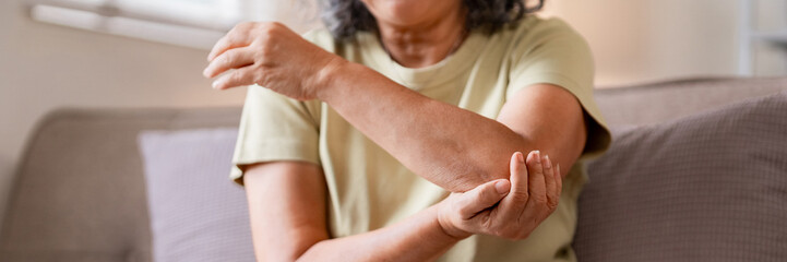 Older Asian woman massage painful elbow home seek relief joint discomfort arthritis symptoms