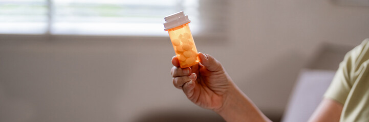 Older adult person hand holding prescription medication bottle daily health management patient care treatment wellness home environment