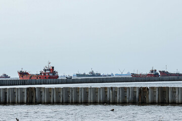 Fishermen and ships activities around the construction of a breakwater for a container port.