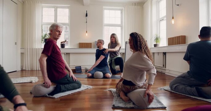 Yoga teacher showing a mixed age range
group of students the seated twist pose during
a beginners yoga class
