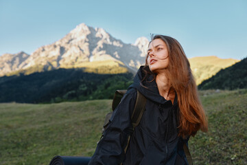 Fototapeta premium A solo hiker woman stands outdoors in a mountainous landscape. She carries a backpack and gazes toward the distant peaks with calm confidence and natural serenity.