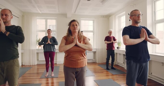 Mixed age range group of students learning the
crescent moon pose with a teacher during a
beginners yoga class