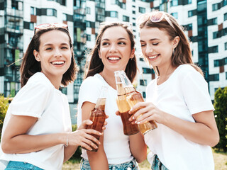 Three young beautiful smiling hipster female in trendy summer same clothes.Sexy carefree women posing in the street.Positive models having fun in sunglasses. Drinking bottle beer. Oktoberfest