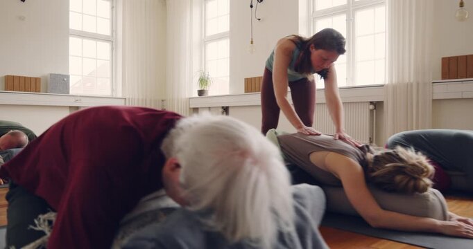 Teacher helping a student using a bolster pillow
with her child's pose during a beginners yoga
class in a studio