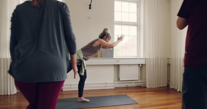 Yoga instructor teaching a diverse group of
students the warrior three pose during a
beginners yoga class in her studio