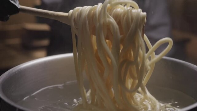 Close-up view of hands of chef stirs the pasta in the pan with boiling water. Preparing Asian udon noodles in a saucepan.