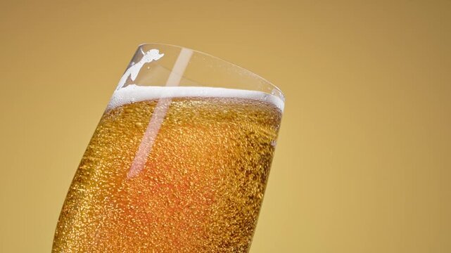 Cold craft light beer pouring in glass from bottle, slow motion close up. Stream wheat malt beverage flowing in clear goblet making dense bubbling foam. Froth heady drink foaming on yellow background