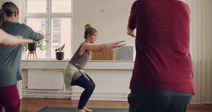 Yoga instructor teaching a diverse group of
students the figure four pose during a
beginners yoga class in her studio