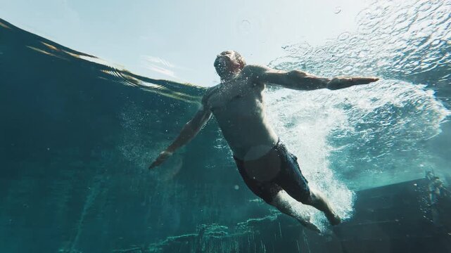 Underwater view of the man jumping and swimming in the crystal clear karst lake. Man dives and glides underwater in the blue lake. The lake named Goluboye Ozero, Samara, Russia
