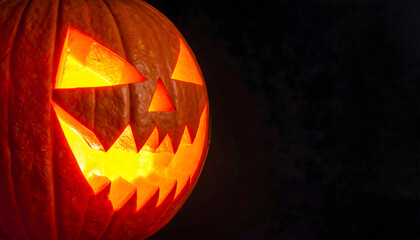 Close up of a carved halloween pumpkin with a scary face glowing from within, set against a dark background